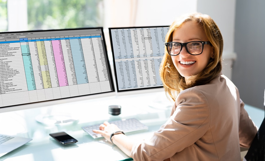 Mujer en escritorio sonrie mientras trabaja en 2 monitores