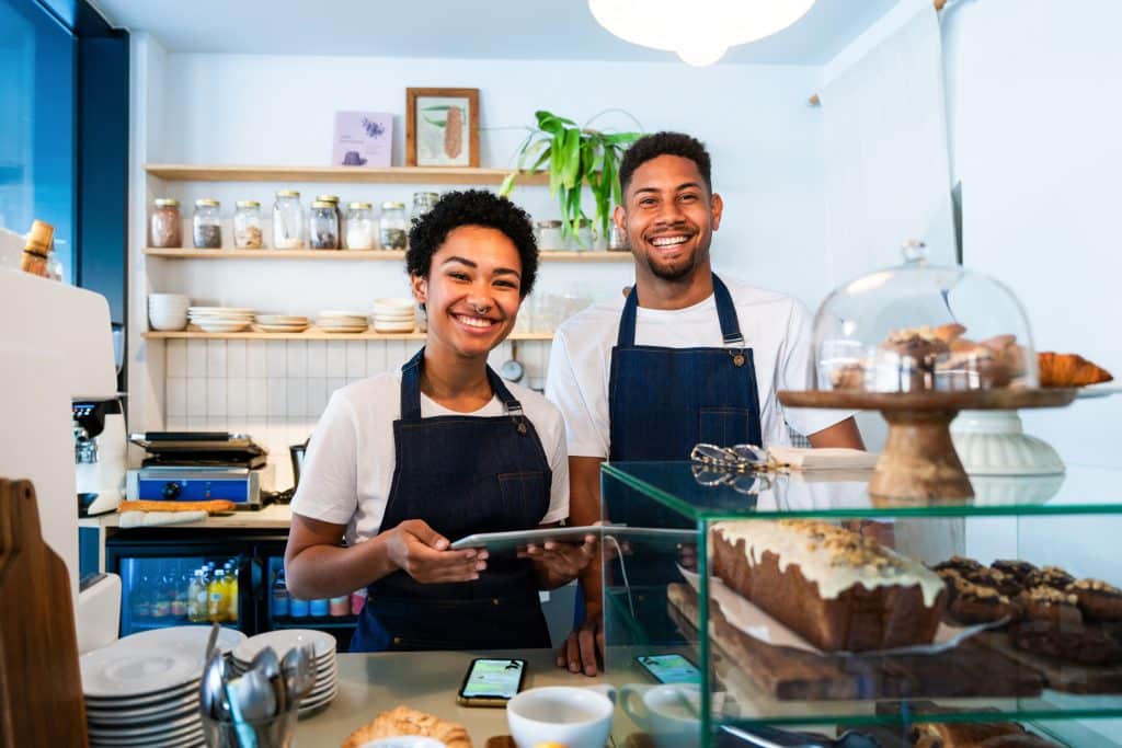 Trabajadores de una cafetería, sonrientes en la barra listos para atender con caja registradora